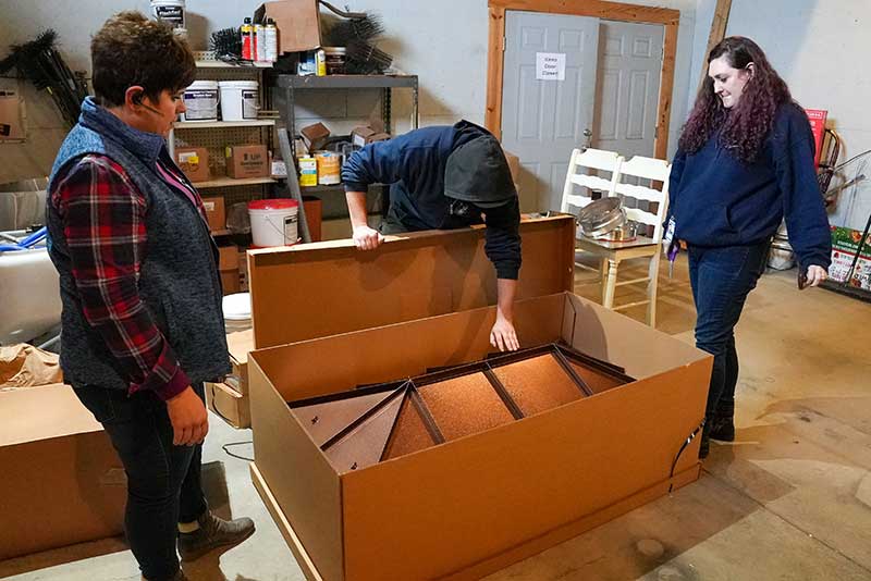 Three people standing around a custom copper chimney cap in a box. 