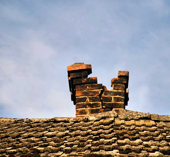 Cracked and crumbling chimney fall apart in half with wooden shingles.