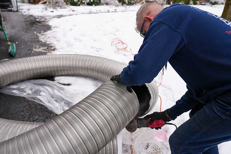 Tech cutting chimney liner with a hand saw with snow in the background.