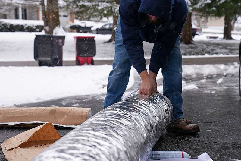 Tech picking up new chimney liner off the ground with snow and trash cans in the background.