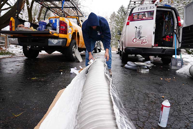 Man unwrapping new chimney liner on driveway with two trucks in background.