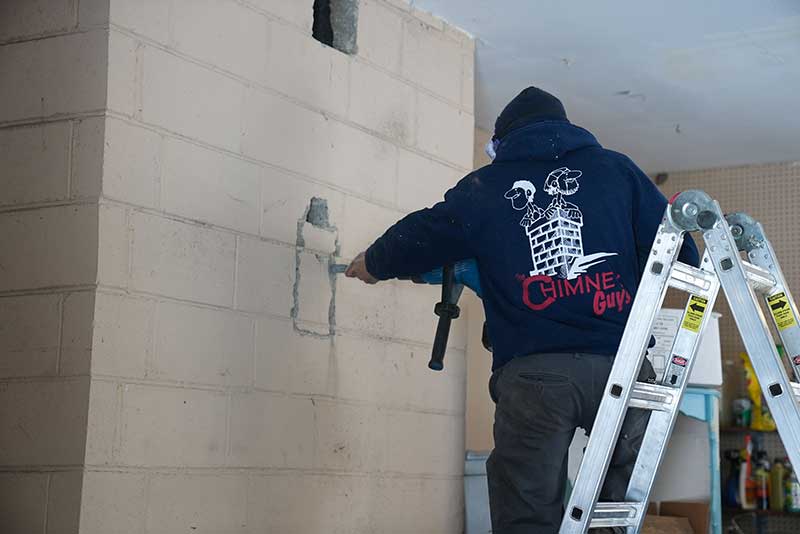 Tech using jigsaw to cut opening in masonry wall standing on ladder.