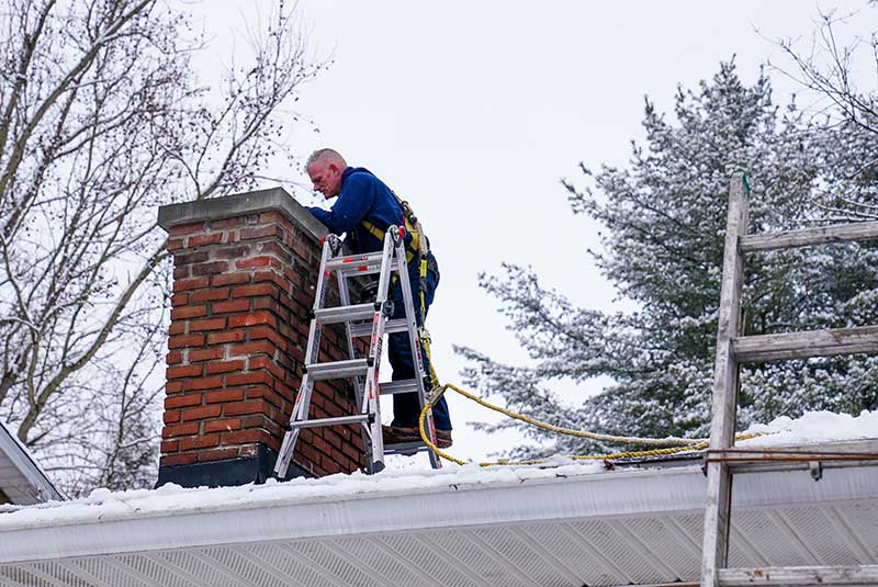 Man wearing safety harness inspecting chimney with ladder.